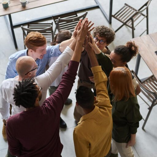 A diverse group of professionals high-fiving in a modern office, showcasing teamwork and collaboration.